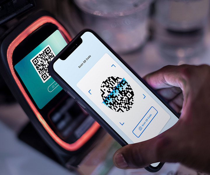 Hand holding a smartphone scanning a QR code on a payment terminal